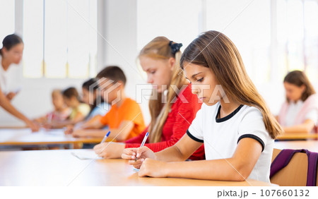 Interested diligent preteen schoolgirl writing exercises at lessons Interested diligent preteen schoolgirl writing exercises at lessons 107660132