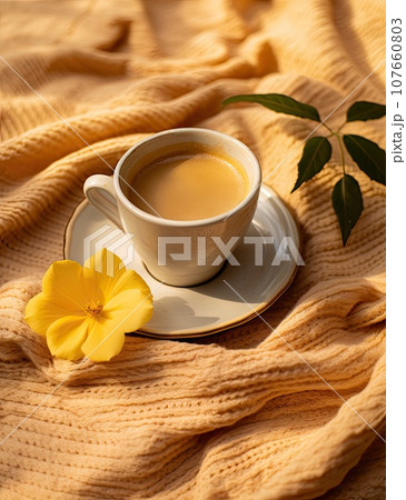 a cup and saucer on a yellow blanket with a flower in the fore photo is taken from above it 107660803