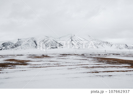 Pastel colors with the snow covered mountains in the distance. Dramatic overcast sky. Severe mountains peaks covered by snow. 107662937