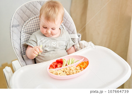 Cute child eats healthy food vegetables and meatballs from dietary meat steamed,. Portraits of a cute 10 months old baby girl. The baby sitting in a special high chair for babies. 107664739