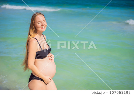 Radiant pregnant woman in a swimsuit, amid the stunning backdrop of a turquoise sea. Serene beauty of maternity by the shore 107665195