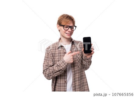 young successful european student man with red short hair and glasses shows the screen of a mobile young successful european student man with red short hair and glasses shows the screen of a mobile 107665856
