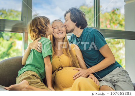 Expectant parents, mom, dad, and their eldest son share a heartwarming moment on the sofa, discussing the exciting journey of pregnancy Expectant parents, mom, dad, and their eldest son share a heartwarming moment on the sofa, discussing the exciting journey of pregnancy 107665882