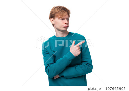 young red-haired man with a blue sweater shows his hand to the side. advertising concept young red-haired man with a blue sweater shows his hand to the side. advertising concept 107665905