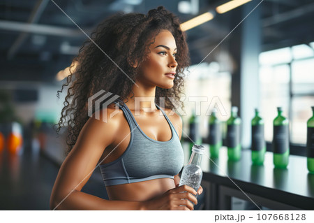 Beautiful young fit woman with a bottle of water after training in the gym 107668128