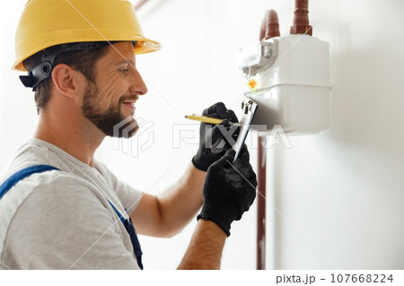 Happy professional heating fitter making notes while checking gas consumption at gas pipe and meter counter 107668224