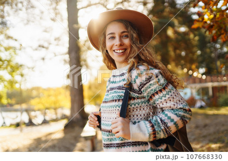 Stylish woman enjoying autumn weather in the sunny park. Enjoying nature. Fashion, style concept. 107668330