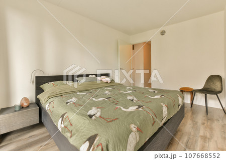 a bed in a room with white walls and wood flooring on the wall, there is a chair next to the bed 107668552