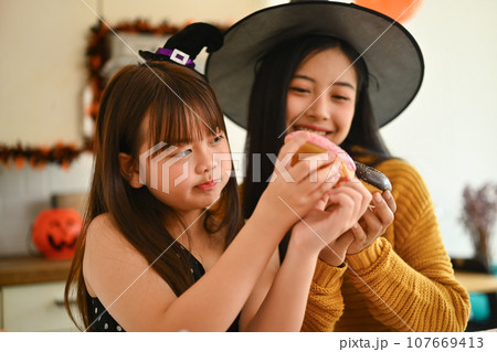 Happy mother and cute girl daughter are having fun preparing Halloween desserts in kitchen Happy mother and cute girl daughter are having fun preparing Halloween desserts in kitchen 107669413