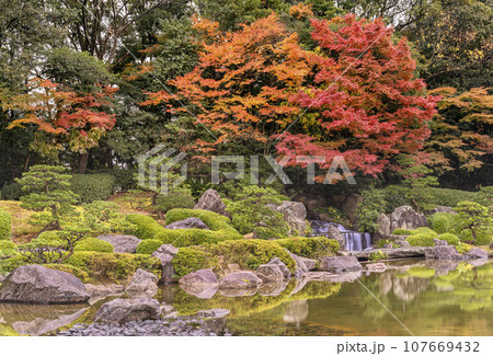 [九州・福岡] 雨の中の紅葉を反射する静かな福岡県立大濠公園日本庭園の池の風景。 107669432