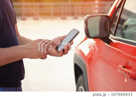 A man uses a mobile phone while standing near his car outdoors. Modern lifestyle A man uses a mobile phone while standing near his car outdoors. Modern lifestyle 107669835