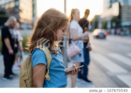 Girl waiting at the pedestrian crossing, scrolling on her smartphone on her way to school. Concept of back to school. Girl waiting at the pedestrian crossing, scrolling on her smartphone on her way to school. Concept of back to school. 107670540