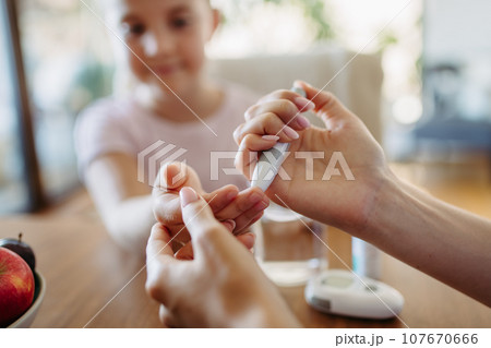 Close up of mother checking girl's blood glucose level using fingerstick glucose meter. Endocrinologist waiting for results from blood test. 107670666