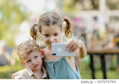 Cousins taking selfie at family garden party. Family reunion at a garden barbecue party. Cousins taking selfie at family garden party. Family reunion at a garden barbecue party. 107670704