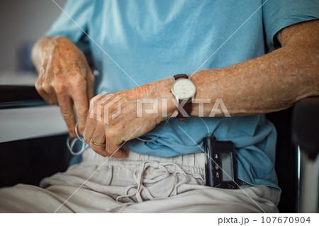 Senior man checking his blood sugar level on insulin pump. Close up of senior man in wheelchair with type 1 diabetes. 107670904