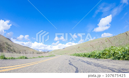 Vehicle is cruising along the Cuyama Highway under the bright sun. The surrounding landscape is illuminated by the radiant sunshine, creating a picturesque and inviting scene as the car travels 107675425