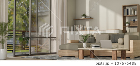 Interior design of a modern living room with a laptop on a coffee table, a grey couch, a balcony. 107675488
