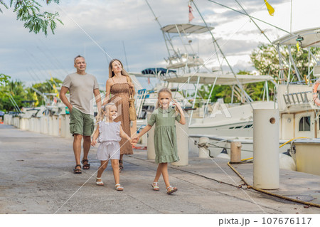 A happy, mature couple over 40 with their two daughters enjoying a leisurely walk on the waterfront, their joy evident as they embrace the journey of pregnancy later in life 107676117