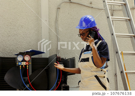 African american apprentice calling manager to inquire about necessary condenser components needing to be replaced. Electrician checking maintenance plan after fixing bad wiring issues African american apprentice calling manager to inquire about necessary condenser components needing to be replaced. Electrician checking maintenance plan after fixing bad wiring issues 107676138