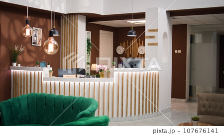 Interior of welcoming rustic hospitality industry hotel lobby filled with plants, waiting for guests. Empty luxurious resort front desk decorated with international timezones on clocks. 107676141