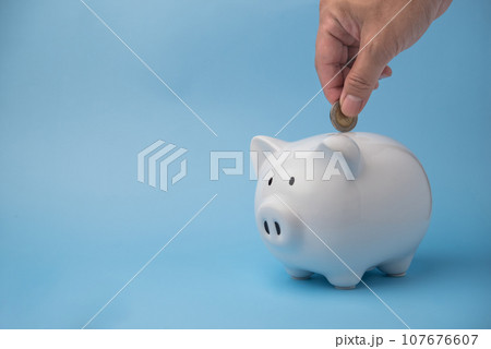 Money management and financial success. Man hand putting coins in a white piggy bank for wealth accumulation and financial independence and investment on background. Money management and financial success. Man hand putting coins in a white piggy bank for wealth accumulation and financial independence and investment on background. 107676607
