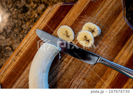 Selective focus on slices of a bananas on a wooden cutting board Selective focus on slices of a bananas on a wooden cutting board 107678730