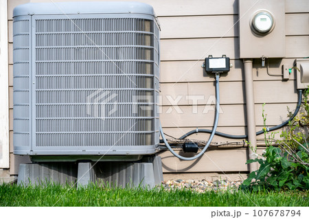 Outdoor residential air conditioner on an elevated pad. Electrical utility hookups on building exterior.  107678794