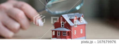 Hand of woman holding magnifier glass above two-story house Hand of woman holding magnifier glass above two-story house 107679976