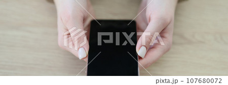 Woman in handcuffs holds modern smartphone sitting at table Woman in handcuffs holds modern smartphone sitting at table 107680072