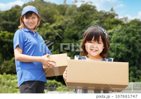 宅配の荷物を届ける。笑顔の子供が段ボールを持っている 107681747