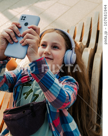 Blonde child in headphones listening to music podcast smartphone outside Young girl learn online lesson enjoy audio book Blonde child in headphones listening to music podcast smartphone outside Young girl learn online lesson enjoy audio book 107681944
