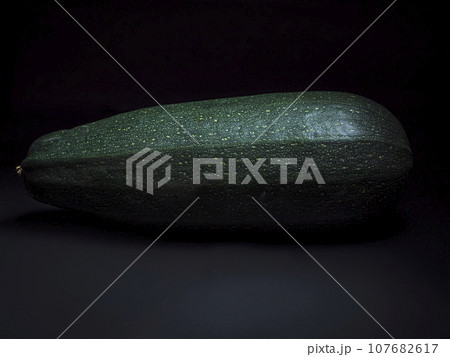 Close-up of a large dark-green zucchini on a dark background Close-up of a large dark-green zucchini on a dark background 107682617