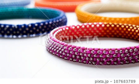 vibrant image of colorful beaded bangles on a white background. The bangles are arranged in a semi-circle, creating a rainbow effect. 107683789