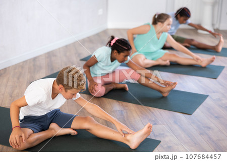 Group of preteen children doing stretching on mats during yoga class Group of preteen children doing stretching on mats during yoga class 107684457