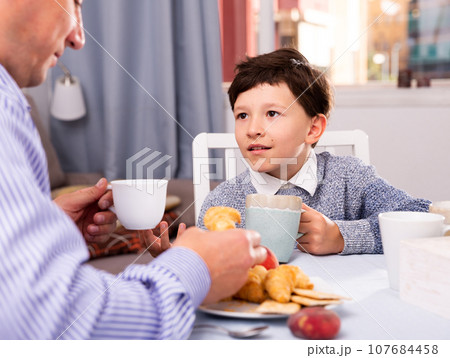 Son chatting with his young father at table with tea indoors 107684458