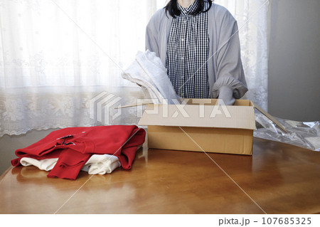 洋服をネットショッピングで購入　早速開封する女性 107685325