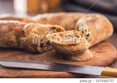 Sliced wholegrain rustical baguette on wooden table. 107686757