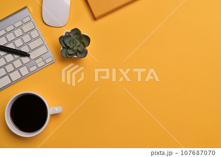 Top view of coffee cup, keyboard and notebook on yellow background. Space for text advertising text message Top view of coffee cup, keyboard and notebook on yellow background. Space for text advertising text message 107687070