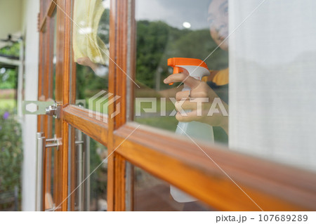 Young Asian housewife cleaning window glass with rags and detergent spray, cleaning house on the weekend 107689289
