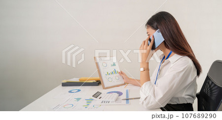 Happy young asian businesswoman talk on the mobile phone while sitting at working place in office 107689290
