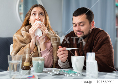 Couple suffering from flu and cough sitting wrapped in blankets 107689911