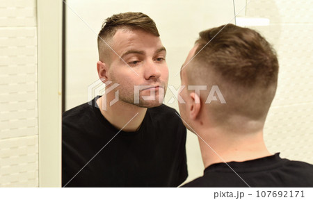 Young man looking in the mirror at his reflection in a bathroom 107692171