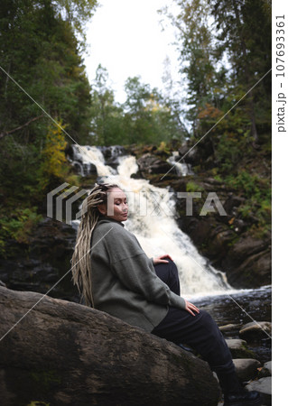 young beautiful Asian woman with African braids against the backdrop of a picturesque waterfall surrounded by forest young beautiful Asian woman with African braids against the backdrop of a picturesque waterfall surrounded by forest 107693361