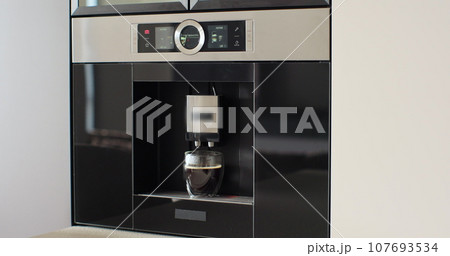 Automatic coffee machine pours coffee into mug in kitchen at home. Hot coffee drink concept. 107693534