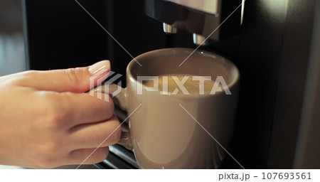 Coffee machine pours coffee into mug. Woman takes the finished drink. Drinking coffee in the morning. Close up. Coffee machine pours coffee into mug. Woman takes the finished drink. Drinking coffee in the morning. Close up. 107693561