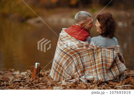 Seen from behind modern couple in park with blanket hugging Seen from behind modern couple in park with blanket hugging 107693919