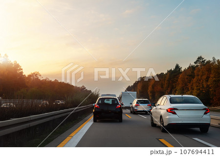 Back tail view of many cars stuck in row at highway city street road traffic jam warm sunset time. Automobile accident vehicle rush hour collapse. Town transport commute infrastructure blockage strike Back tail view of many cars stuck in row at highway city street road traffic jam warm sunset time. Automobile accident vehicle rush hour collapse. Town transport commute infrastructure blockage strike 107694411