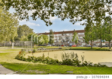 an empty park in the middle of a residential area, with trees and grass growing on either side of the road 107694844