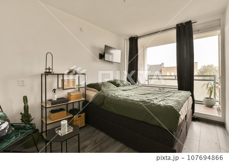a bedroom with a bed, desk and tv on the wall in front of the window looking out onto the street a bedroom with a bed, desk and tv on the wall in front of the window looking out onto the street 107694866