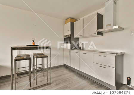 a kitchen and dining area in a modern apartment with white walls, wood flooring and stainless steel bar stools a kitchen and dining area in a modern apartment with white walls, wood flooring and stainless steel bar stools 107694872